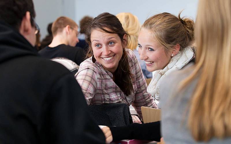 Eine Studierende und eine Schülerin drehen sich um und lächeln