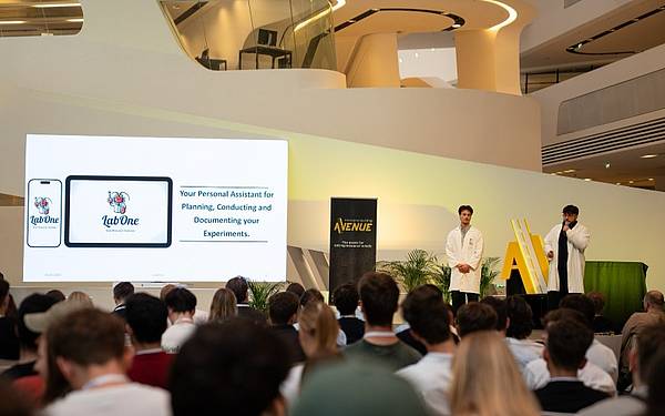 Zwei junge Männer stehen auf einer Bühne, im Vordergrund sind Menschen zu sehen