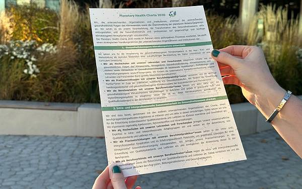 Zwei Hände halten ein DIN-A4-Blatt mit der Überschrift „Planetary Health Charta 2030“.