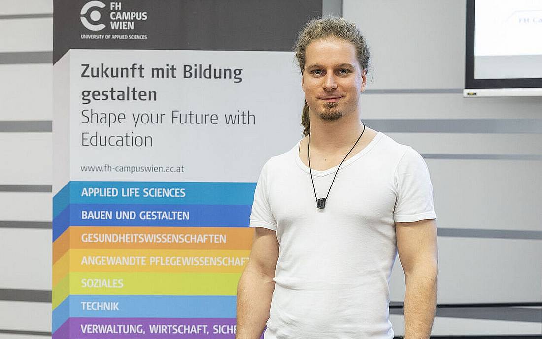 Einer der StartUp-Gründer*innen steht vor einem Banner der Hochschule Campus Wien