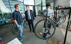 Vor der FH Campus Wien werden Fahrräder gecheckt. Bezirksvorsteher unterhält sich dazu mit einem Mann.