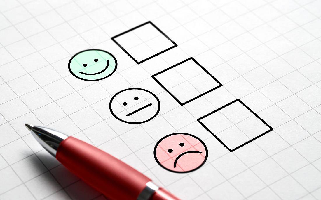 © iStock.com / Tero Ein Stift liegt auf einem Papier neben 3 gezeichneten Emojis, von fröhlich bis traurig, zum Ankreuzen.