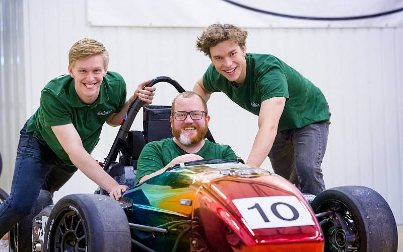 Mitglieder des Oscar Racing Teams lehnen an einem Rennauto