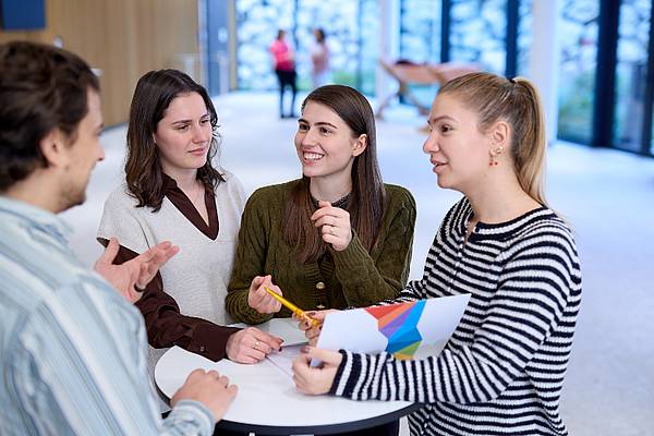 © Hochschule Campus Wien/Schedl Vier junge Menschen stehen rund um einen Tisch.