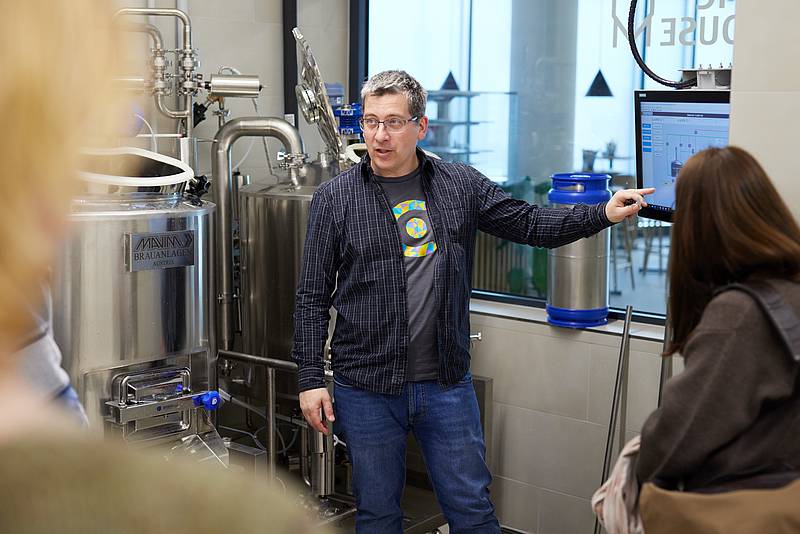 Ein Lehrender des Scientific Brewhouses der Hochschule Campus Wien erklärt den Brauprozess vor einem großen Braukessel. 