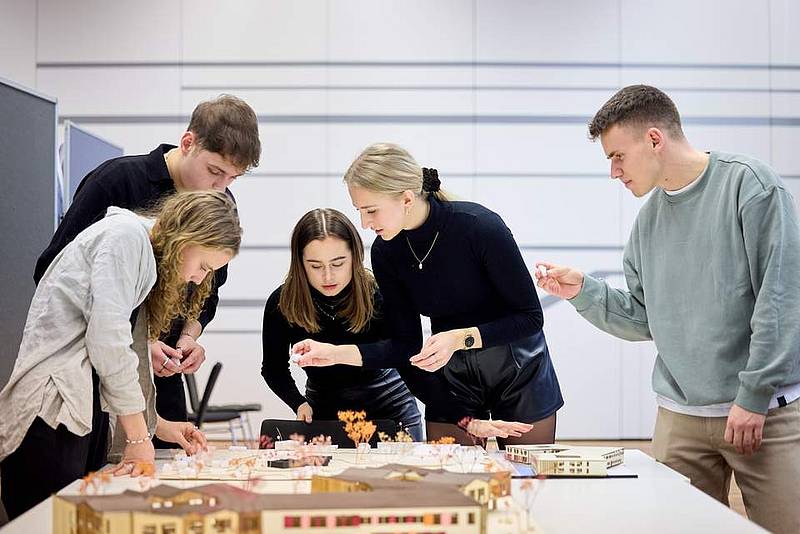 Eine Gruppe steht um ein Architekturmodell und diskutiert dieses