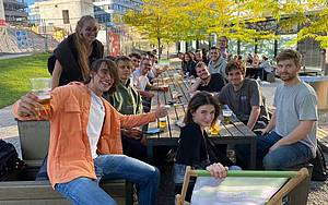 Eine Gruppe Studierende sitzen im Mensagarten an einem Tisch und unterhalten sich