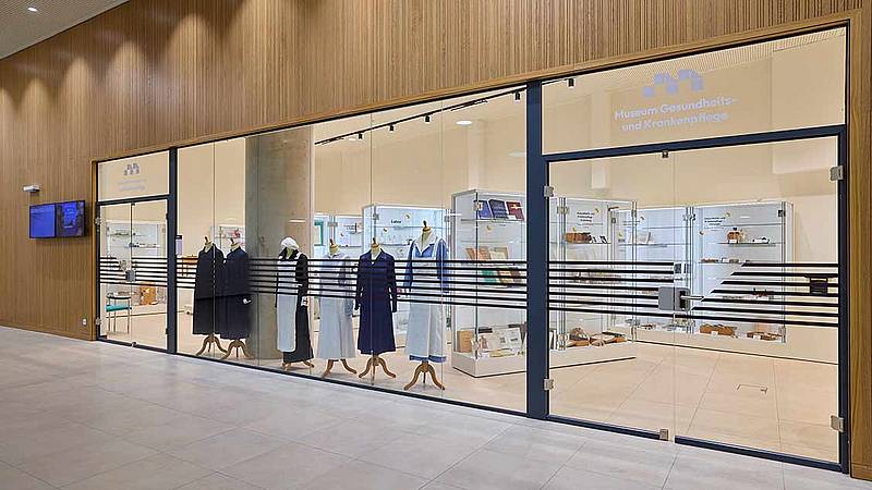 Große Schaufenster und Eingang zum Museum im Gebäude der Hochschule Campus Wien. Vitrinen und unterschiedliche Dienstkleidungen aus der Krankenpflege