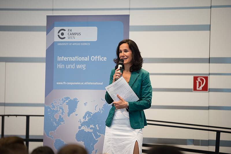 Dame in weißem Rock und grünem Blazer mit Mikrofon in der rechten Hand