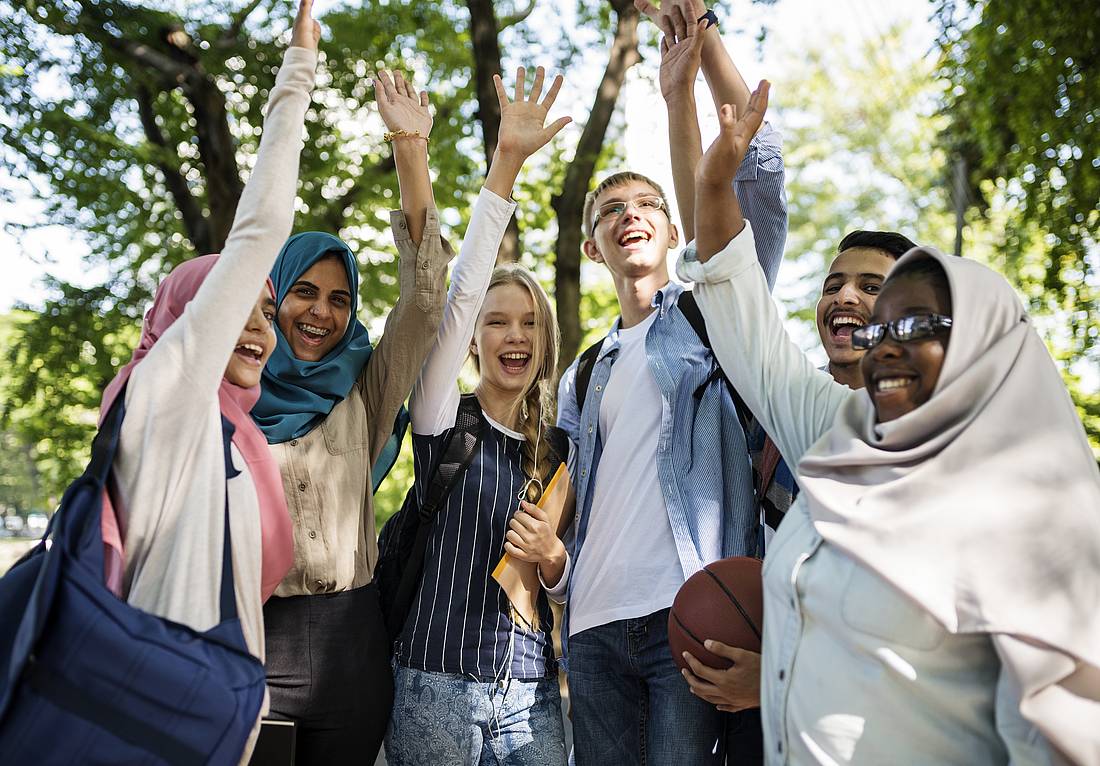 Fünf Personen stehen in einem Halbkreis vor Bäumen. Alle heben einen Arm zum abklatschen.