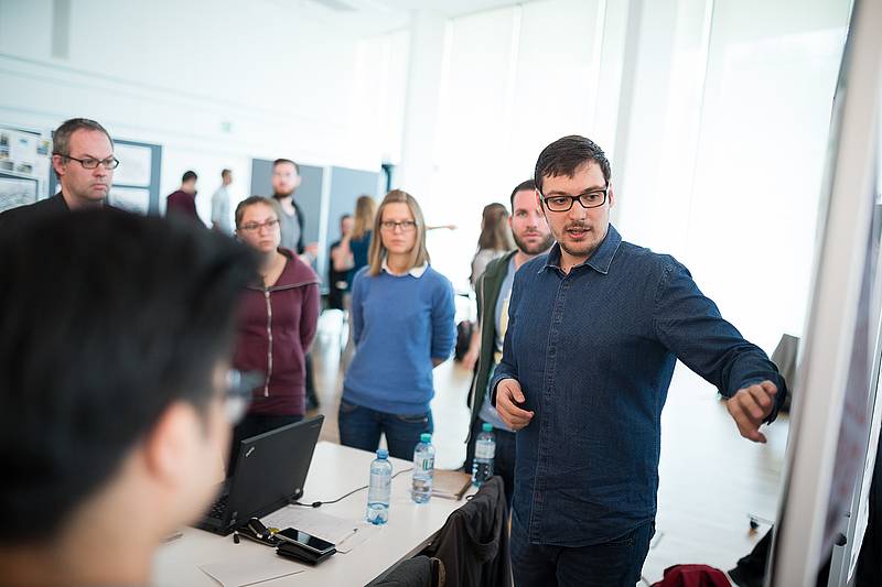 Herr mit Brille präsentiert an Flipchart vor einer Gruppe stehender Personen
