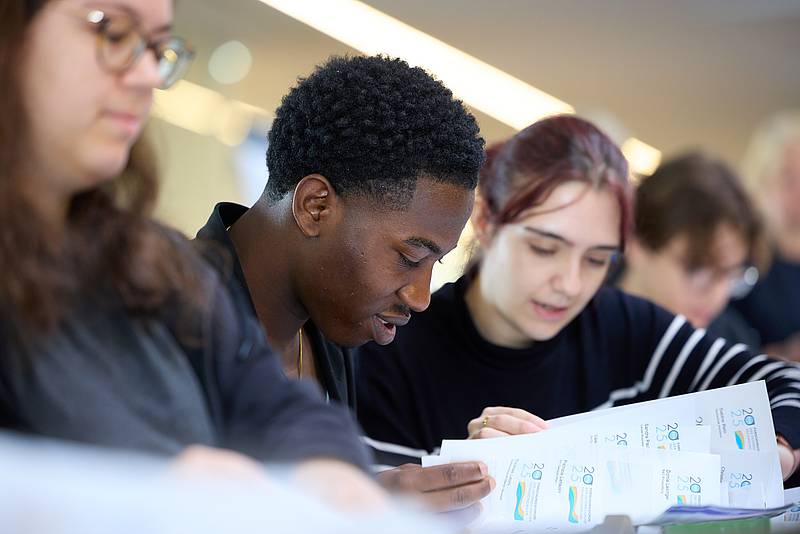 Studierende blättern gemeinsam durch Unterlagen zum Forschungsforum