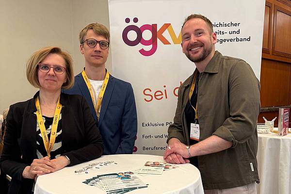 © HCW/privat eine weibliche und zwei männliche Personen stehen an einem Stehtisch vor einem RollUp des ÖGKV
