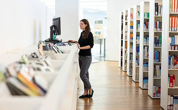Eine Person steht in der Bibliothek vor einem PC-Bildschirm