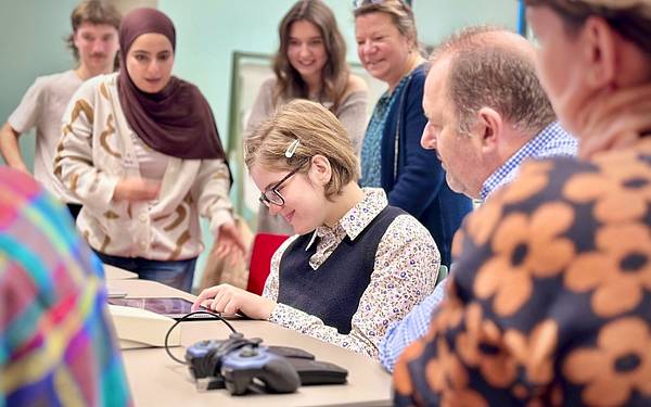 Personen sitzen an einem Tisch und schauen in ein Tablet