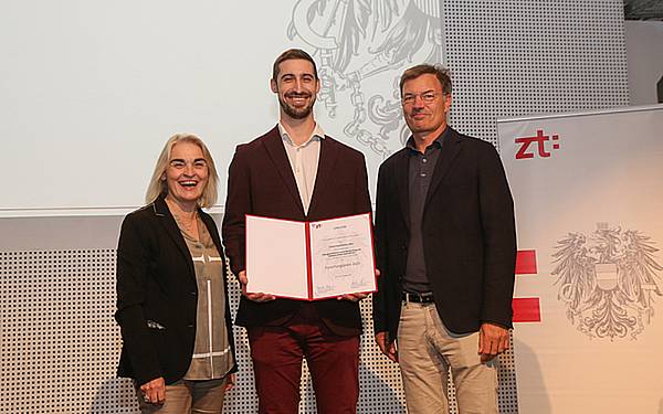 Junger Mann (Simon Kaufmann) hält strahlend seine Urkunde in die Kamera.