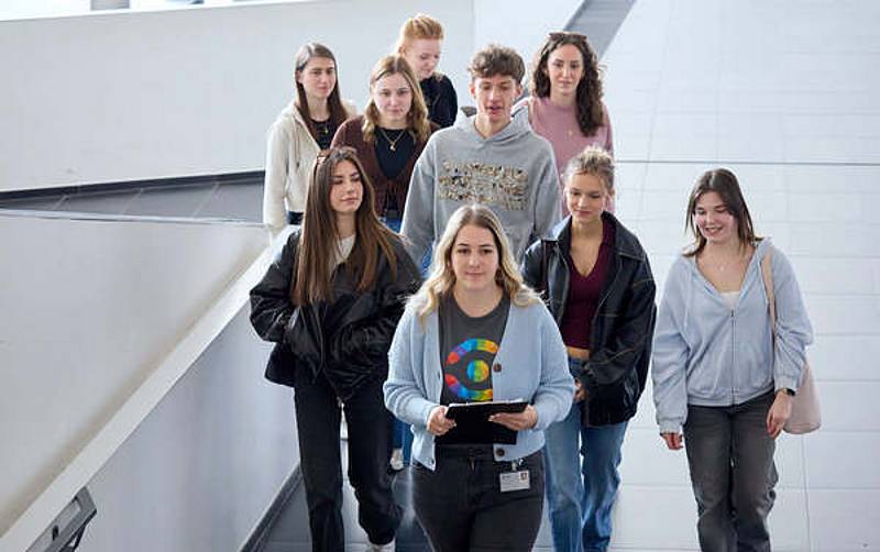 Gruppe von jungen Menschen bei einer Hausführung gehen den Gang entlang