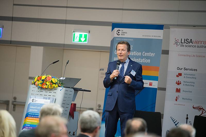 Herr in dunkel blauem Anzug mit Mikrofon vor Publikum