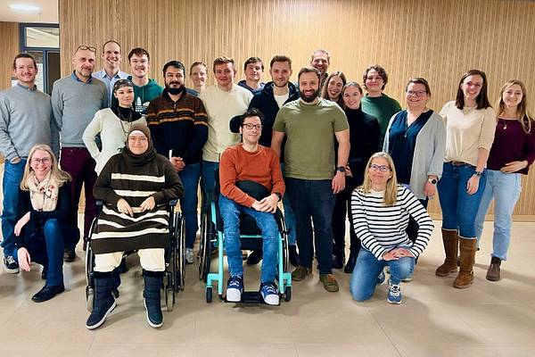 Eine große Gruppe an Menschen posiert vor einer Holzwand