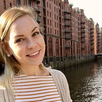 Am linken Bildrand eine junge Frau, die in die Kamera blickt. Im Hintergrund die Speicherstadt in Hamburg.