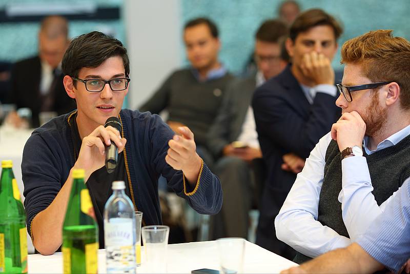 Zwei Männer bei Podiumsdiskussion, einer mit Mikrofon