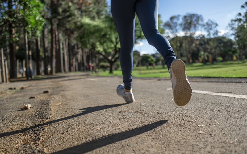 Eine Frau läuft am Rand eines Parks entlang, zu sehen sind nur ihre Beine.