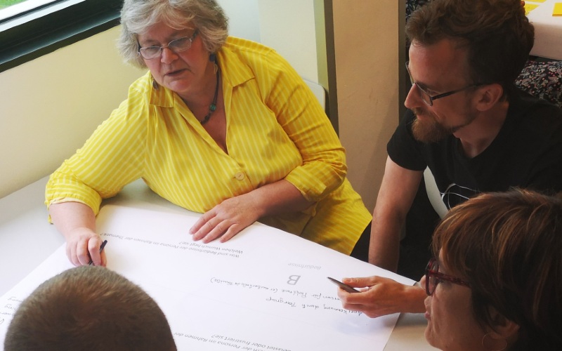 Eine Gruppe hat sich um einem Tisch versammelt und ist im Gespräch vertieft