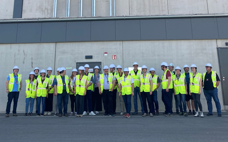 © HCW / Meischl Eine Gruppe von Personen mit Warnwesten und Arbeitsschutzhelmen vor einem industriellen Gebäude