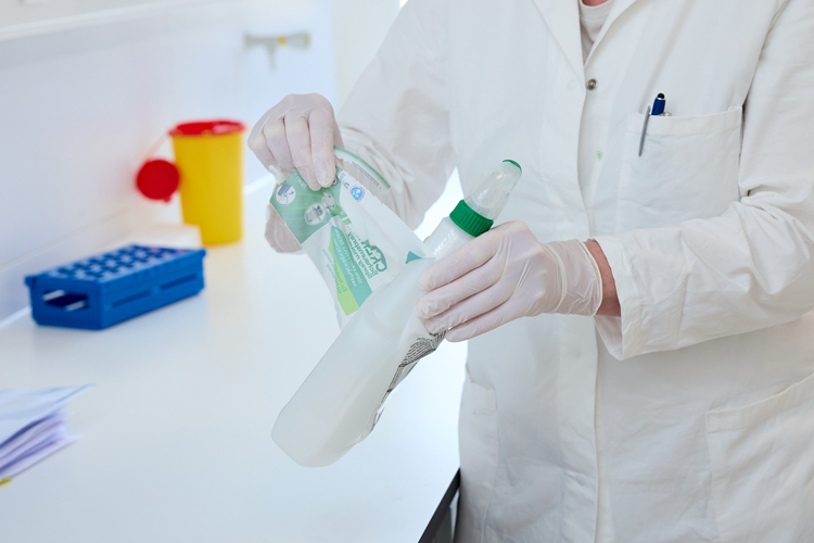 Eine Person in Laborkittel und mit Einweghandschuhen zieht eine Schrumpffolie von einer Plastikverpackung ab