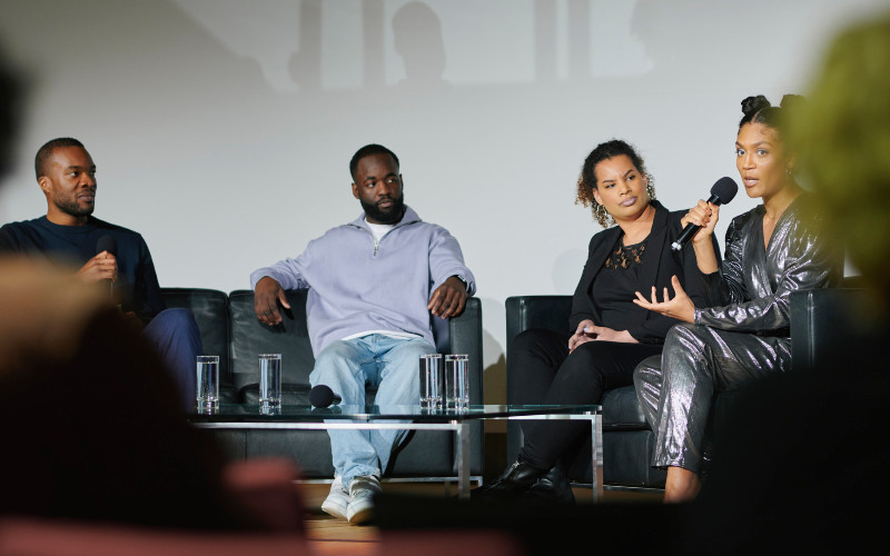 Eine Gruppe Sitzt in Sesseln auf einer Bühne und spricht durch ein Mikrofon