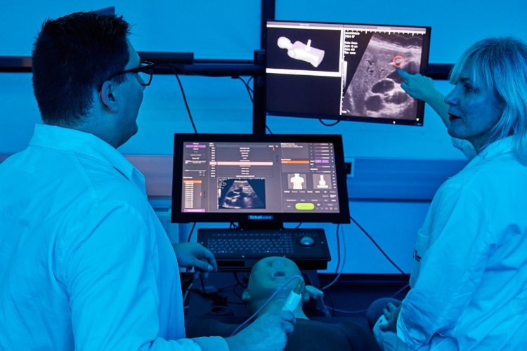 Zwei Personen beim Ultraschall an einem Dummy zeigen auf Bildschirme und sprechen mit einander