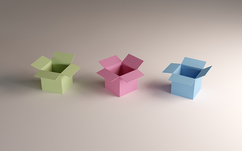 Drei kleine, geöffnete Kartonboxen sind in einer Reihe Positioniert. Die Linke ist grün, die Mittlere rosa und die Rechte blau.