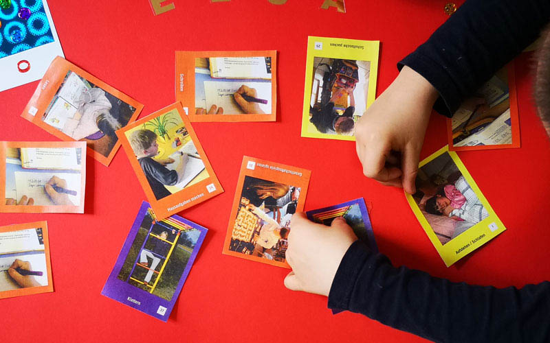 Auf roter Oberfläche liegen Spielkarten verteilt, jemand spielt mit den Karten