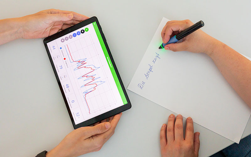 Person hält Tablet in der Hand Kind schreibt auf einem Blatt Papier