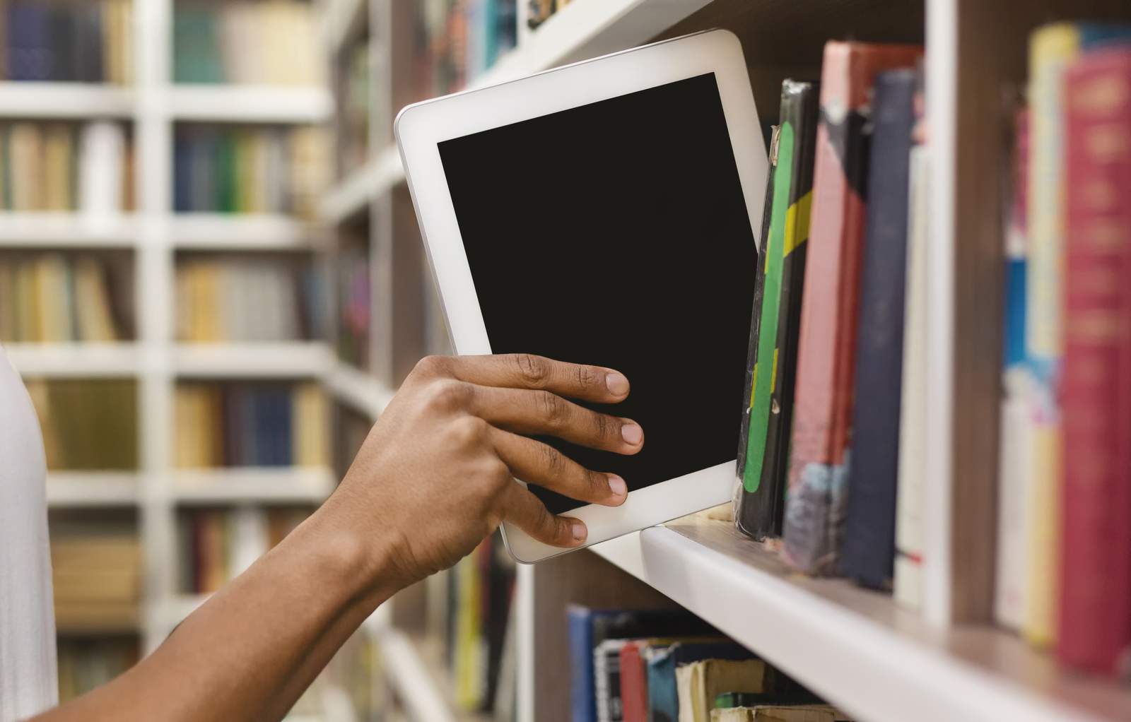 Eine Hand greift nach einem Tablet in einem Bücherregal