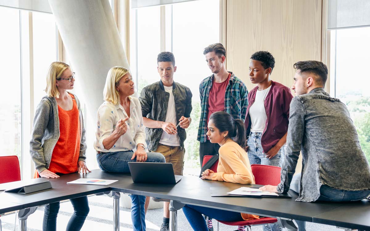 Eine Gruppe von Student*innen und eine erläuternde Dozentin stehen um einen Laptop
