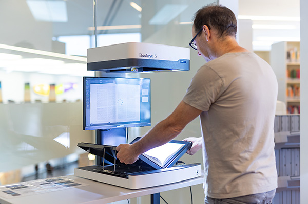 Eine Person verwendet den Buchscanner mit einem aufgeschlagenen Buch.