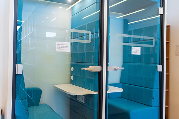 Blick durch die Glastüren der Micro-büros, die etwa so groß sind, wie eine Telefonzelle. Darin ist eine Sitzmöglichkeit und eine kleine Ablage.