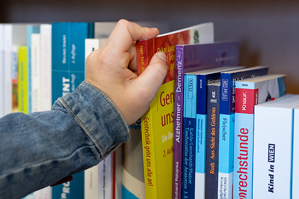Eine Hand zieht ein Buch aus einem Bücherregal heraus.