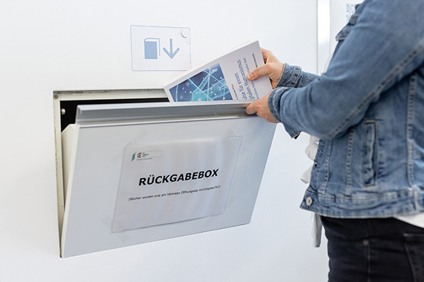 Eine Person wirft ein Buch in die deklarierte Rückgabeklappe