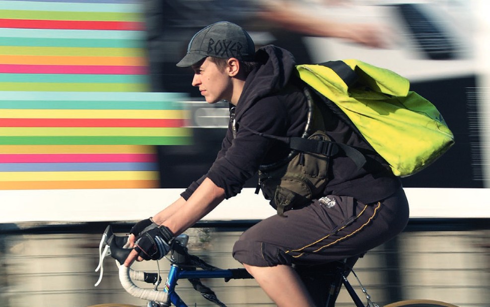 Person on a racing bike with a yellow backpack, shorts and cap