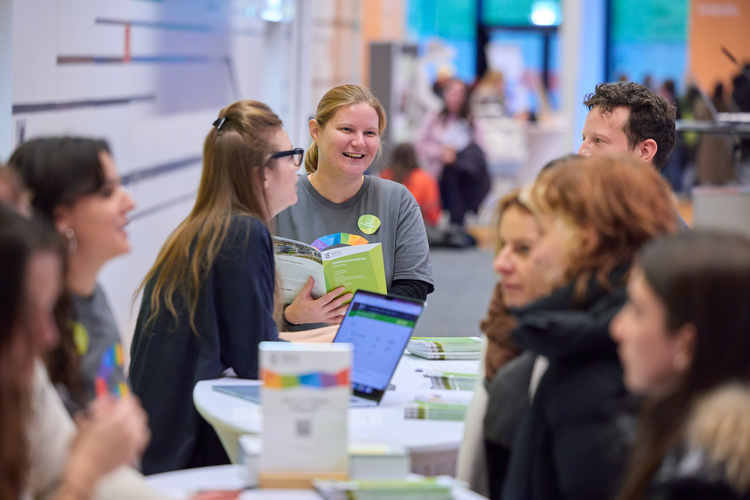 Personen mit T-Shirt der Hochschule Campus Wien an einem Stehtisch im Festsaal. Sie beraten Studieninteressierte.