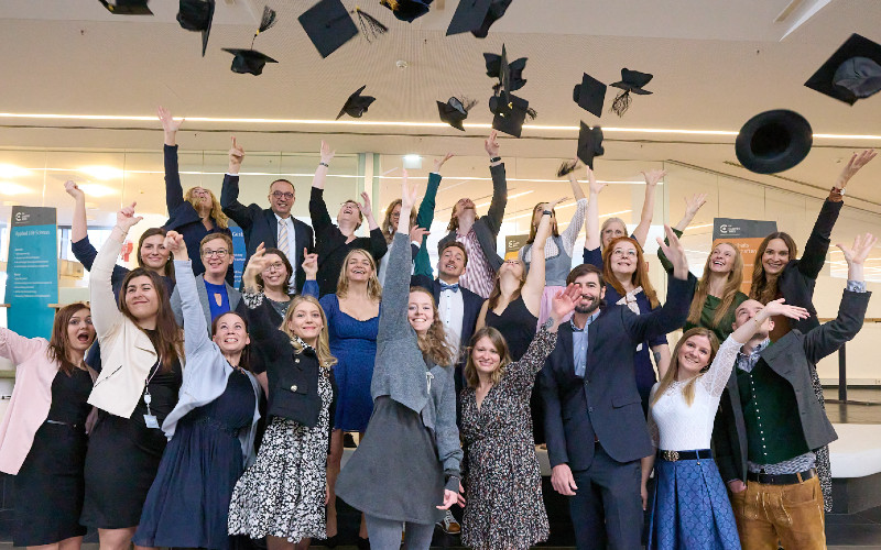 Männer und Frauen stehen und werfen Masterhüte in die Luft