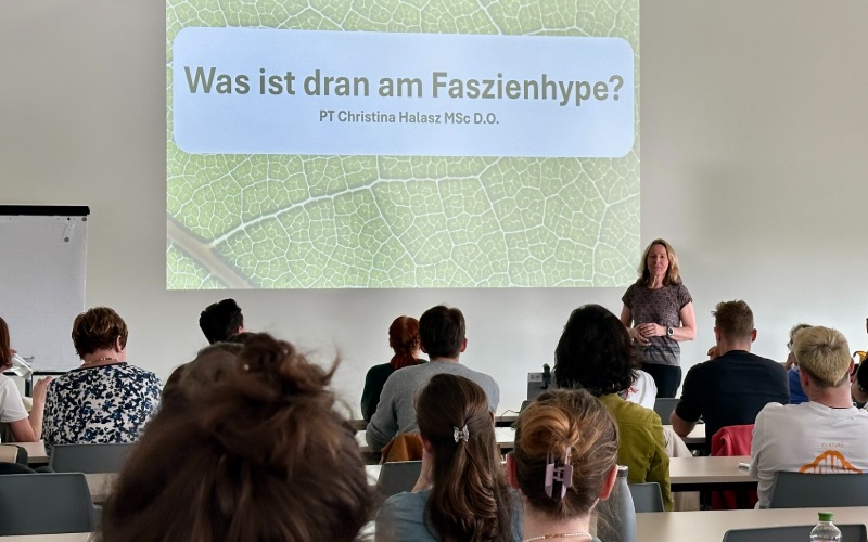 Personen sitzen in einem Lehrsaal und schauen auf eine Präsentation
