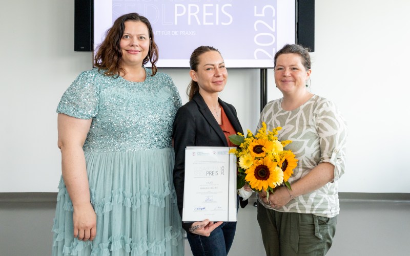 Drei Personen mit Blumenstrauß und Urkunde