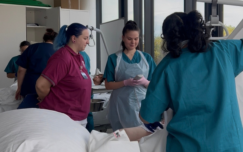 © Hochschule Campus Wien / K. Jagoditsch Gesundheits- undKrankenpflege-Studierenden stehen mit einer Praxisanleiterin vor einem Bett mit einem/einer Patienten/Patientin