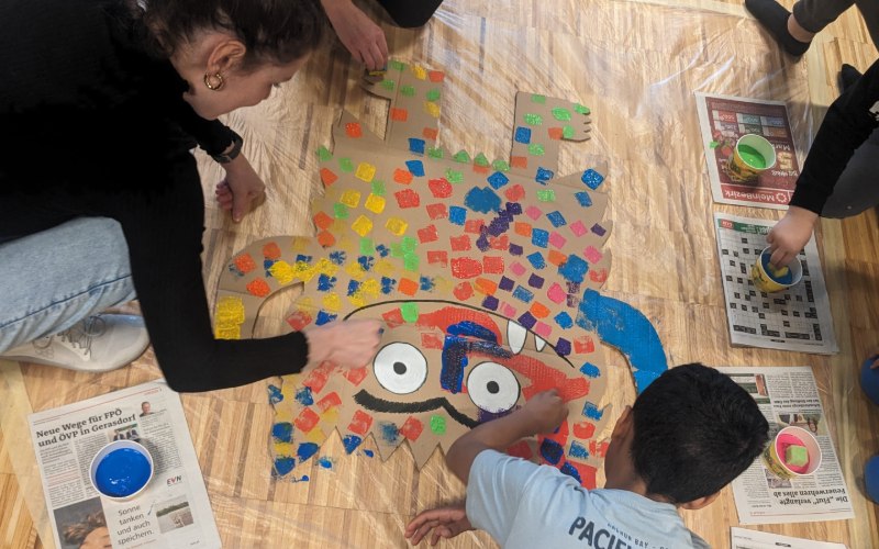 Zwei Kinder von hinten am Boden, die etwas basteln