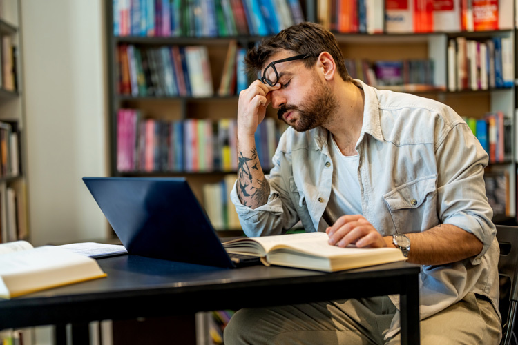 Ein Mann sitzt vor einem Laptop und greift sich merklich genervt an die Stern