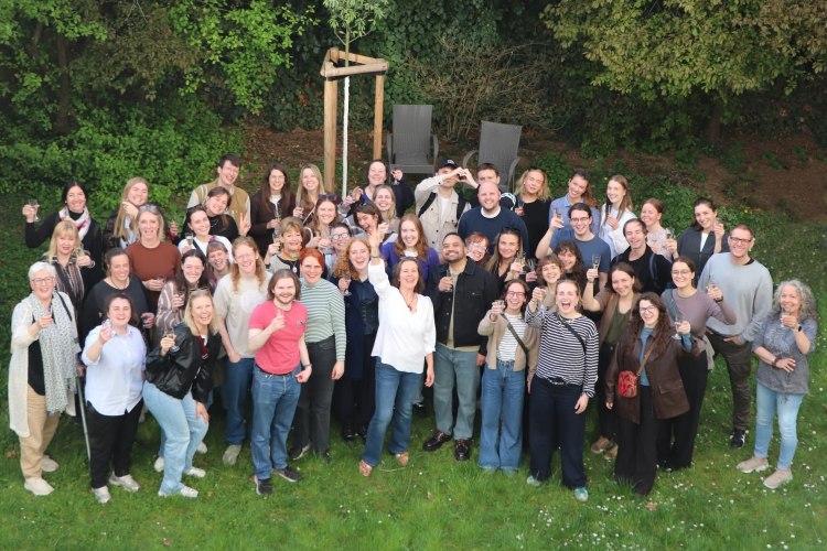 Guppe von Menschen auf Wiese, dahinter Wald