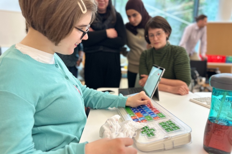 © HCW Eine Person arbeitet an einer Tastatur, im Hintergrund sind verschwommen andere Menschen zu sehen